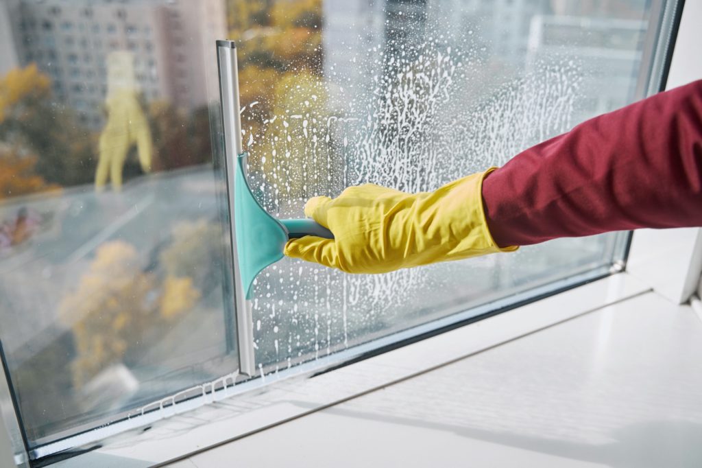 Window cleaner washing windowpane using implement with rubber blade